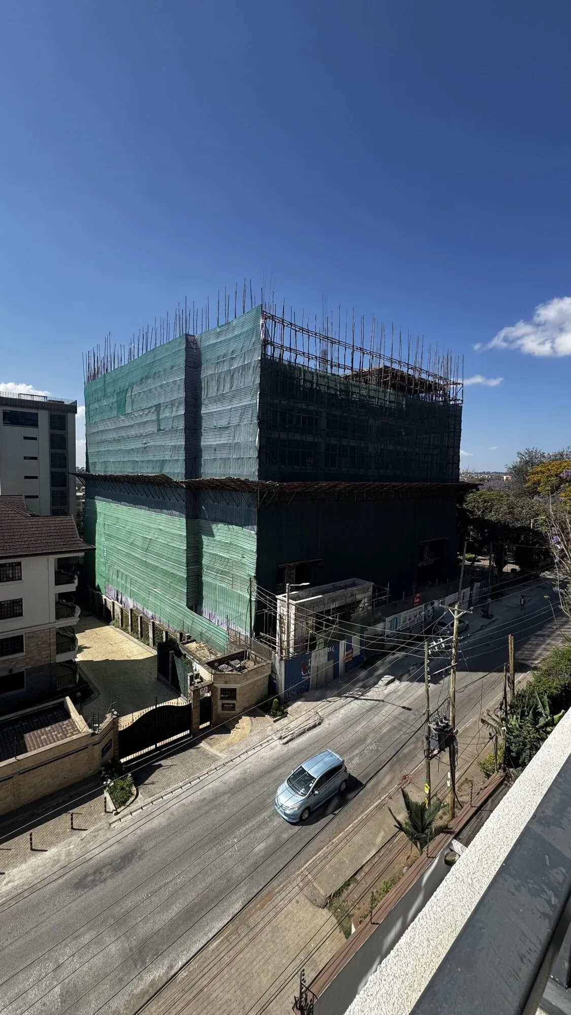 The frame of the building rising above the street, wrapped in green safety netting